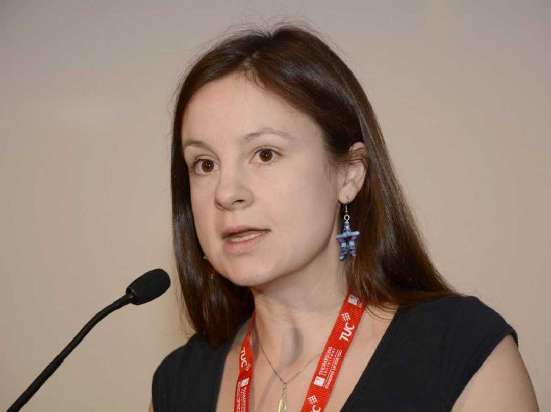 Photo of me addressing TUC from podium (headshot, red TUC lanyard visible as I speak into microphone looking a bit serious)